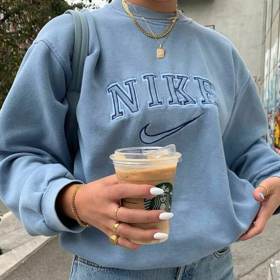 Light blue nike swoosh embroidered sweatshirt worn by a girl posing in a stylish outfit.