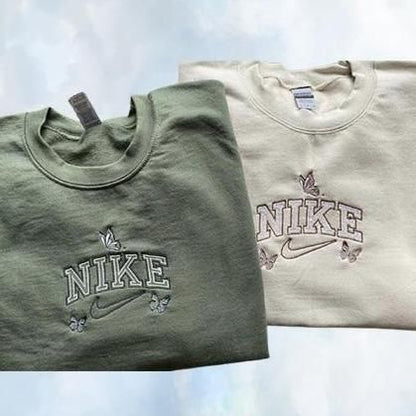 The butterfly outline nike crewnecks in olive green and beige colors laid out together.