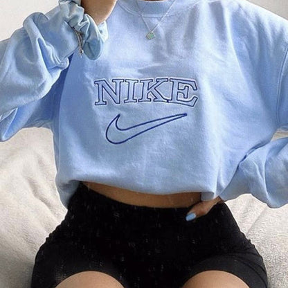 The oversized vintage tick embroidered Nike sweatshirt in light blue with dark blue embroidery worn by a girl.