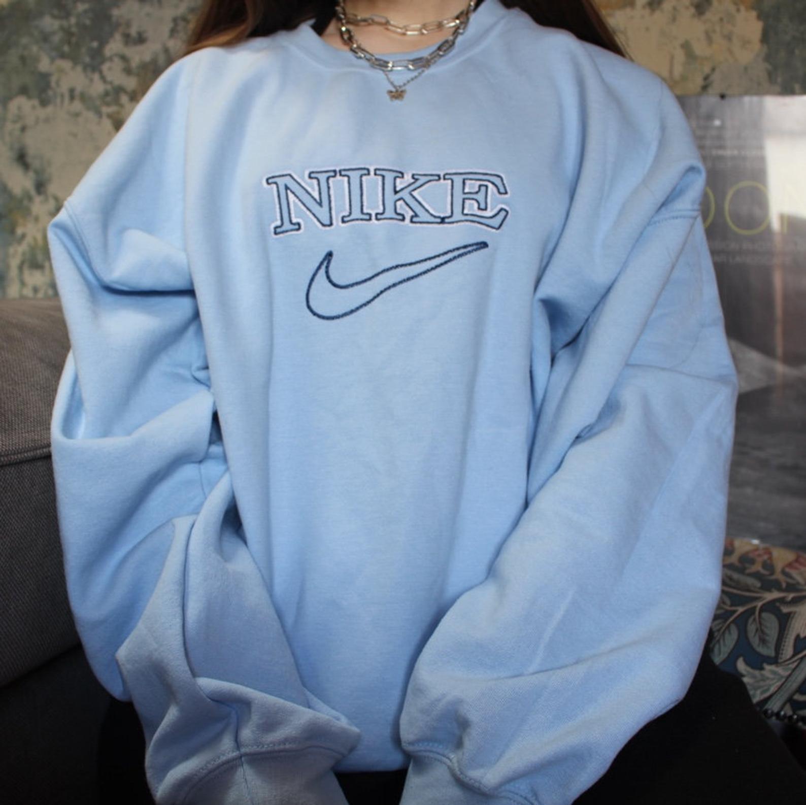 The oversized vintage tick embroidered Nike sweatshirt in light blue with dark blue embroidery worn by a girl.