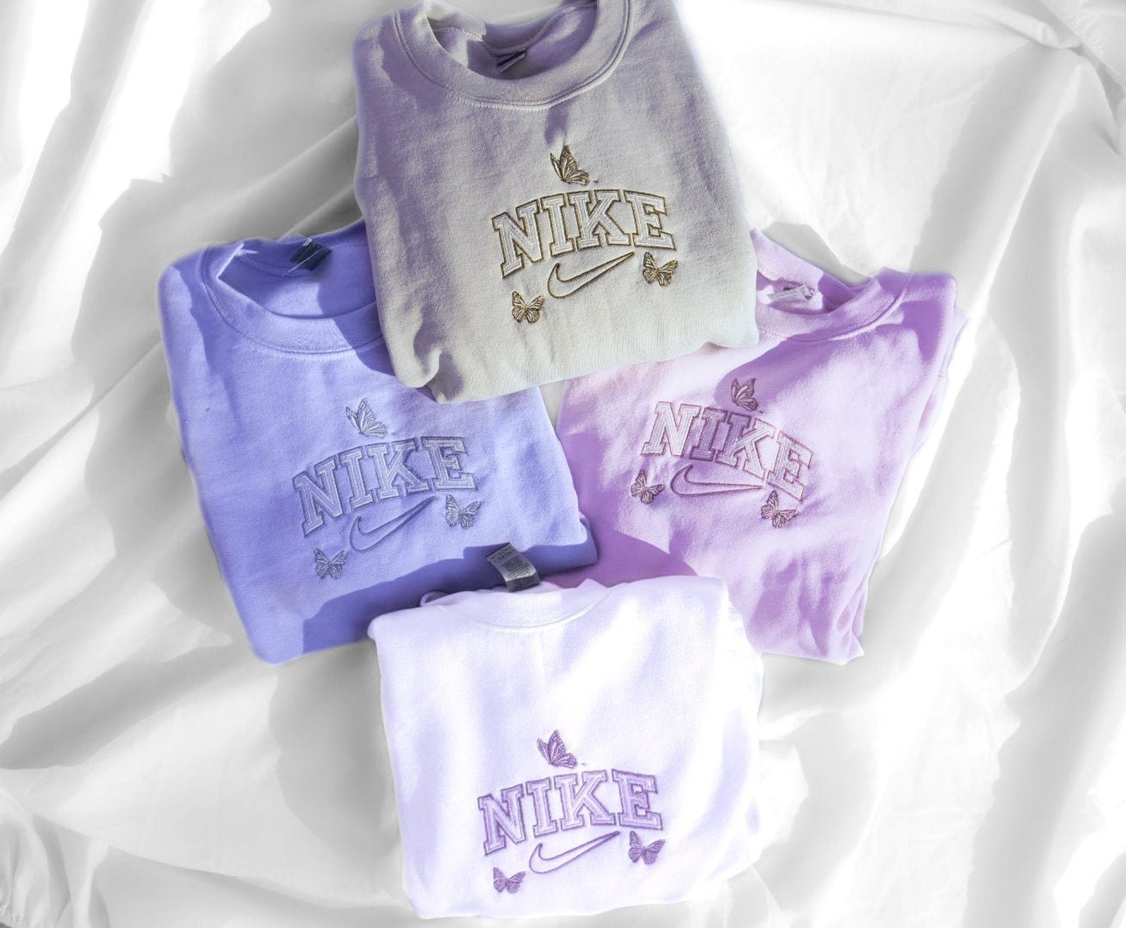 Trendy nike butterfly embroidered crewnecks in blue, purple, and white displayed on white background.