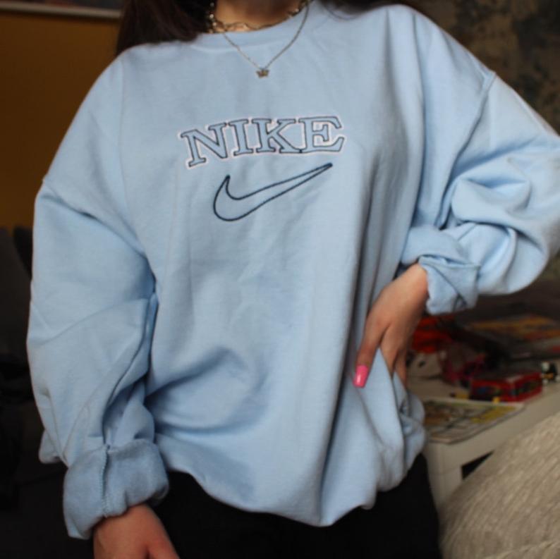 The oversized vintage tick embroidered Nike sweatshirt in light blue with dark blue embroidery worn by a girl.