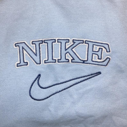 Close up of the oversized vintage tick embroidered Nike sweatshirt in light blue with dark blue embroidery worn by a girl.